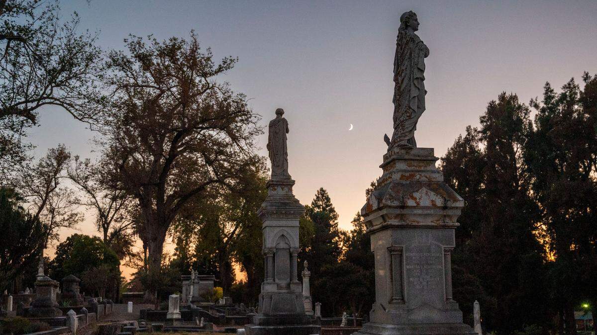 Statue monuments stand in family plots under a crescent moon at the Old City Cemetery on Wednesday, Oct. 19, 2023, that dates to mid-19th century. The cemetery was added to the National Register of Historic Places in 2014.