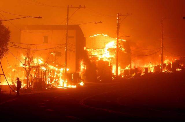 A man stands along Pacific Coast Highway as the Palisades fire burns houses in Malibu on Tuesday, Jan. 7, 2025.