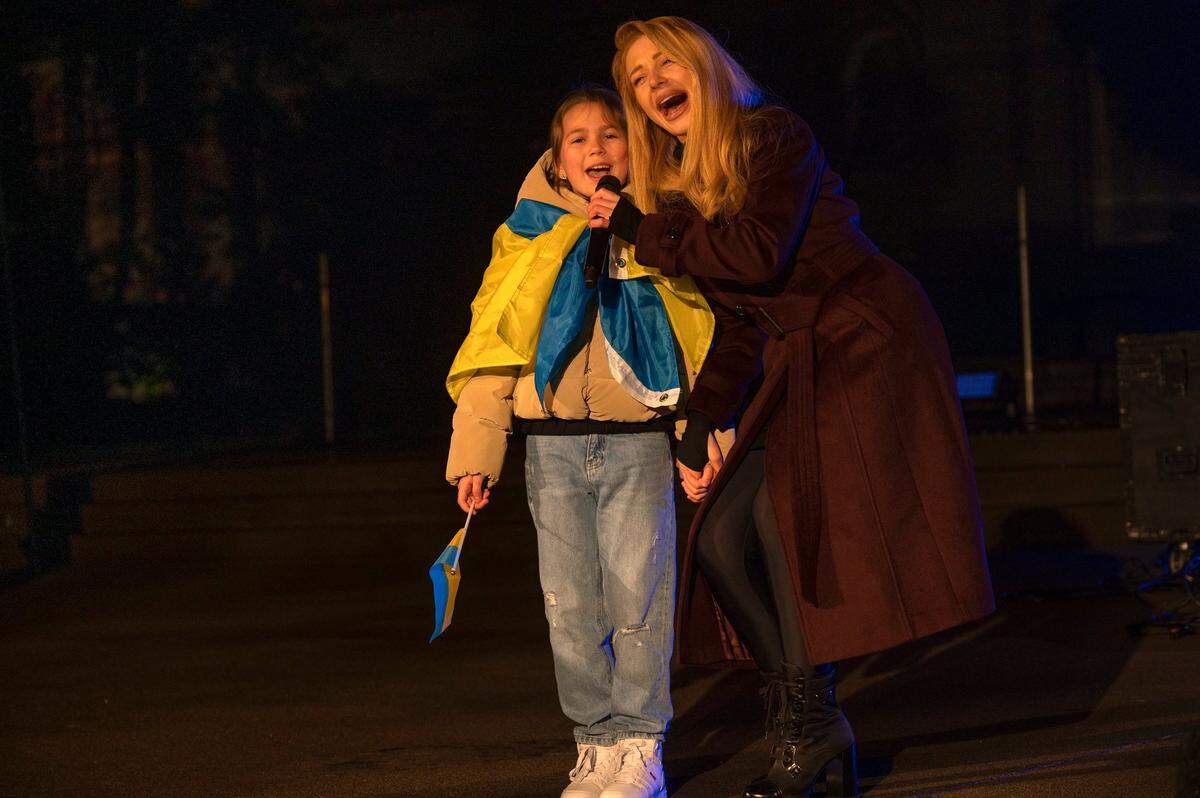 Ukrainian singer Tina Karol joins voices with a girl wrapped in the Ukrainian flag at a rally to mark the one-year anniversary of the Russian invasion of Ukraine at the state Capitol on Friday.