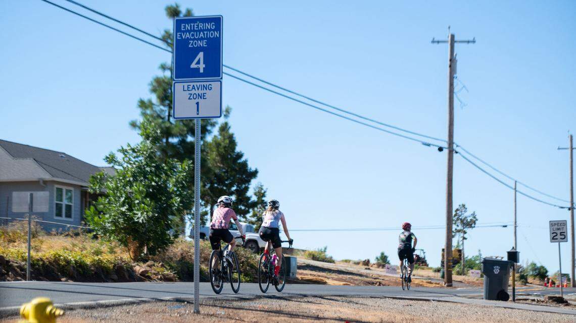 Cyclists ride past an evacuation zone warning sign near Bille Park in Paradise on Friday. The Park Fire, burning to the north, is the biggest fire in California so far this year.