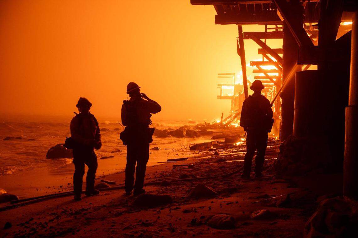 Firefighters battle the Palisades Fire from the surf as beachfront homes go up in flames along Pacific Coast Highway in Malibu on Tuesday, Jan. 7, 2025.
