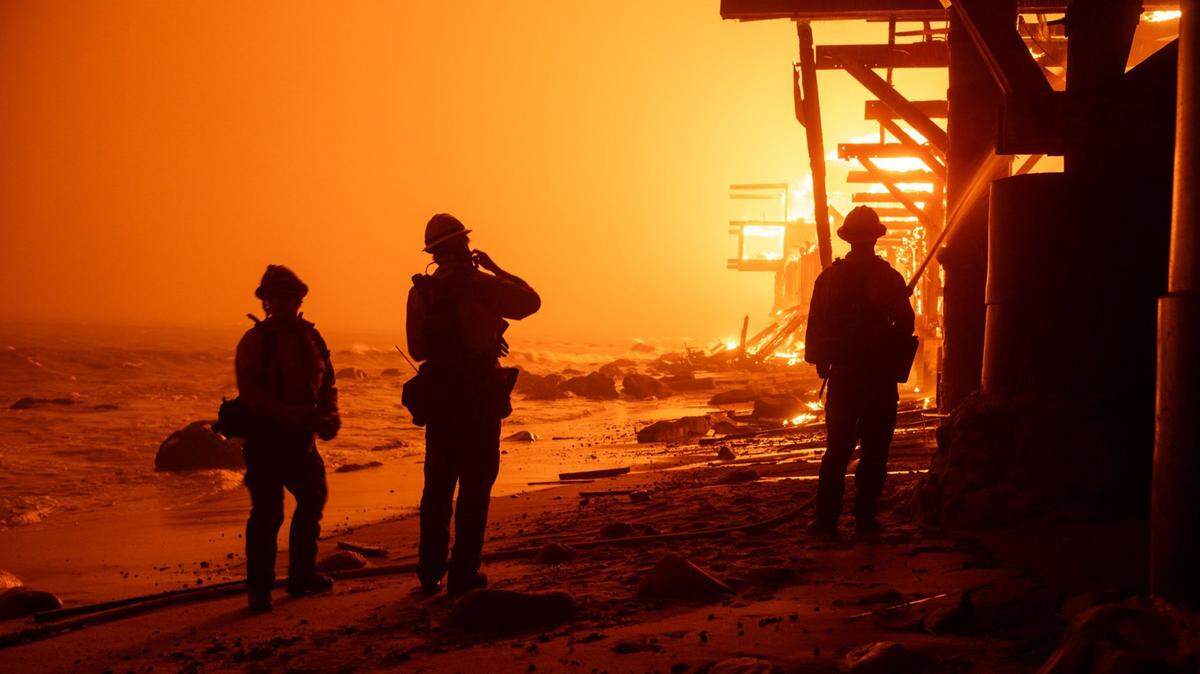 Firefighters battle the Palisades Fire from the surf as beachfront homes go up in flames along Pacific Coast Highway in Malibu on Tuesday, Jan. 7, 2025.