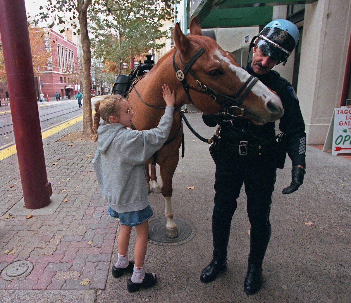 Billy Lyons, a Sacramento mounted patrol officer, keeps a close watch on his horse, Loot, while Rachel Meconit, 9, pats the animal in 2000.