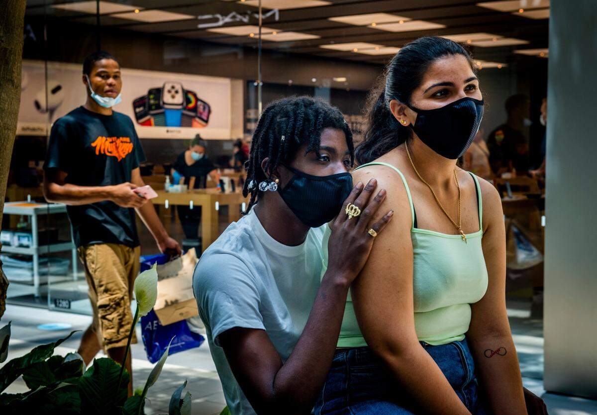 Sacramento resident Nico Clark, 20, middle, holds Amna Barakat, 20, as they sit together wearing masks while waiting for a phone to be repaired at Arden Fair mall on Tuesday, June 23, 2020. Spot checks by The Bee in Sacramento County this week found broad compliance with the governor’s order to wear masks in nearly all outdoor and indoor settings to slow the spread of the coronavirus.