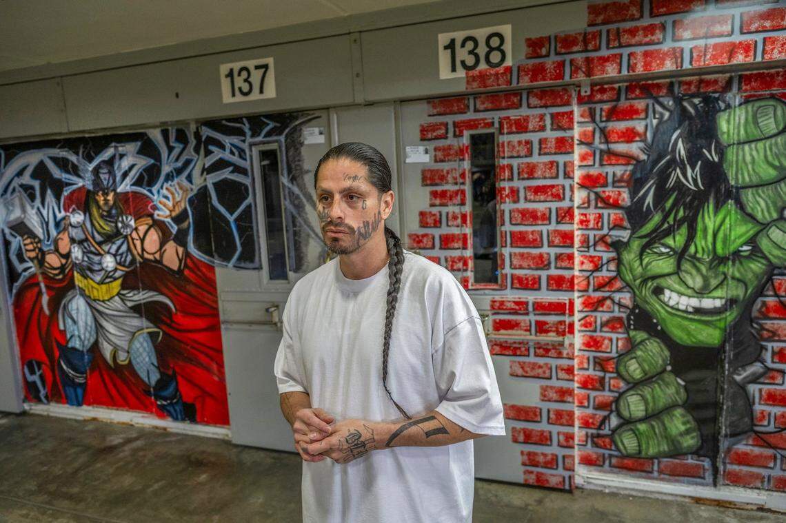 Isaac Sandoval stands last month near murals of superheros he painted in B Ward at Salinas Valley State Prison. “Being in prison, this is self therapeutic for me. Painting and drawing, it helped me to realign back in my community and do something more positive,” Sandoval said.