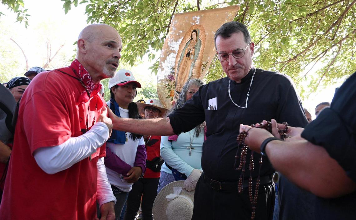 Daniel Orellana-Rogers, left, crosses himself after receiving a beaded rosary from Catholic Bishop Joseph V. Brennan, right, after the marchers reached the day’s final destination in Calwa.