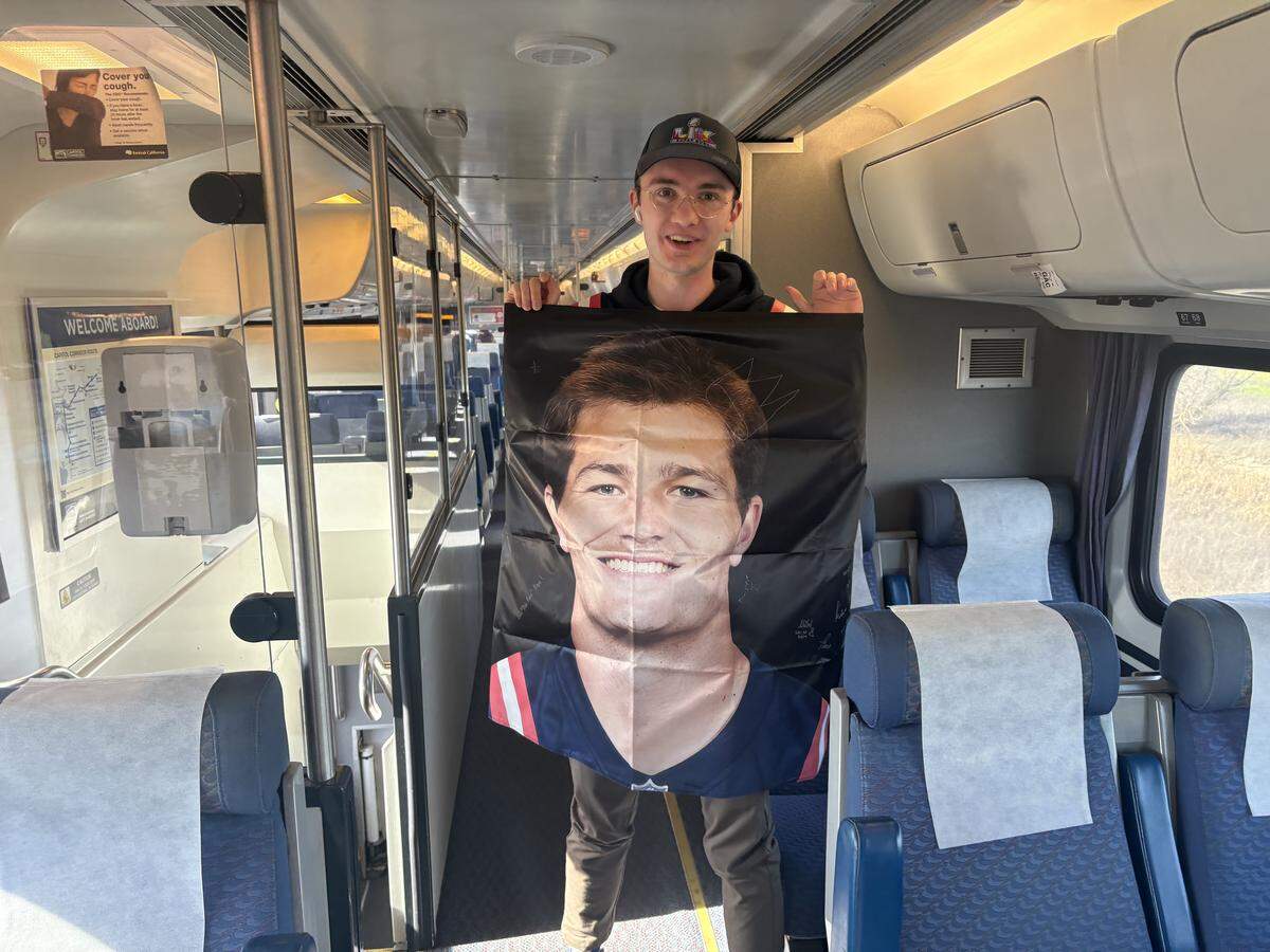 Zach Fillmore, 22, a middle school teacher from New England, holds up a banner of Patriots quarterback Drake Maye as he rides the Amtrak train from where his relatives live in Sacramento to Santa Clara to watch Super Bowl LX on Sunday, Feb. 8, 2026.