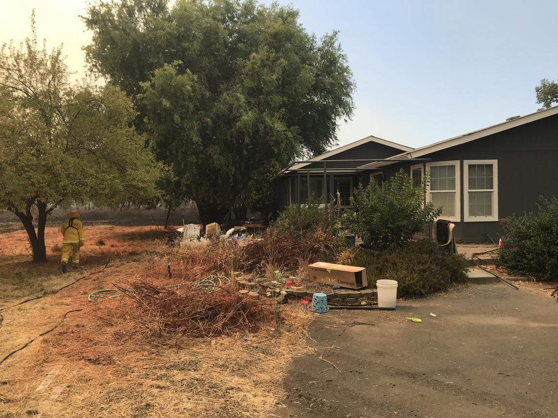 A firefighter with Cal Fire assesses the property of Elizabeth and David Mills on Hendricks Road outside Lakeport. A fire that raged through the area Tuesday came within a few feet of the home, but the house was not damaged.