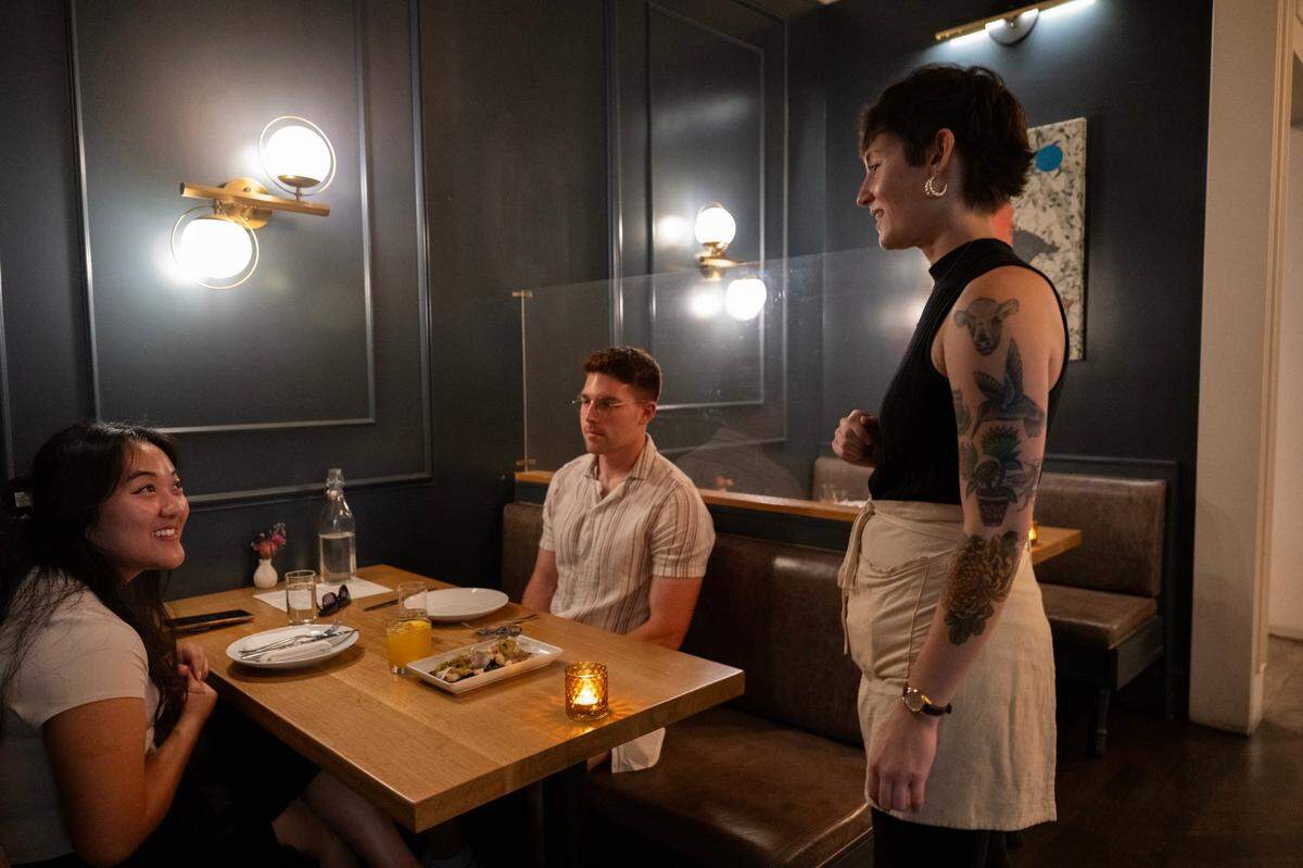 Waitperson Katie Bradley serves Naomi Tanaka and Weston Jones at Canon on Tuesday in East Sacramento. Surcharges have become commonplace at California restaurants but they’ll be banned under a new state law taking effect July 1.