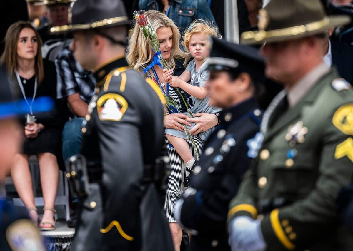 Rachel Gibson, wife of fallen Sacramento Sheriff’s Deputy Adam Gibson, holds daughter Sophie as they place a flower for him Monday, May 2, 2022, during the annual ceremony to add names to the California Peace Officers Memorial at the state Capitol in downtown Sacramento. Gibson was fatally shot at Cal Expo in January 2021.