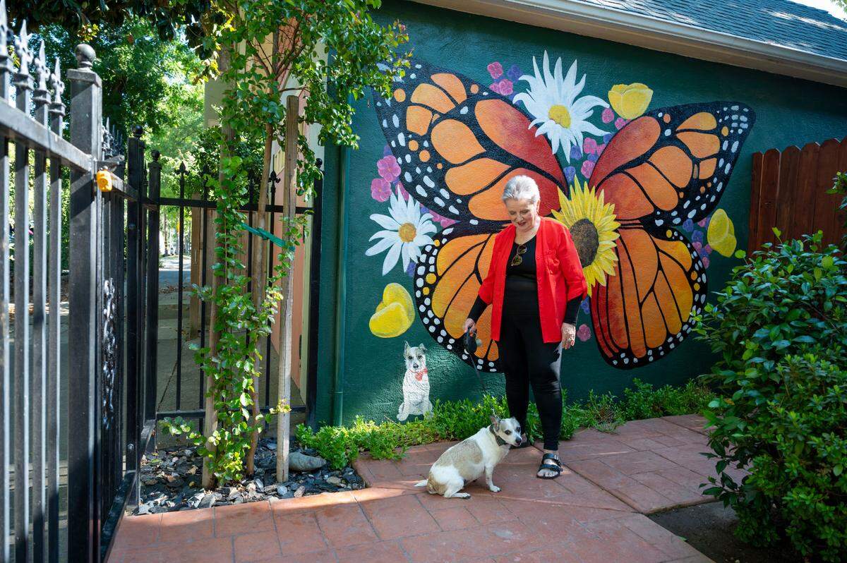 Rebekah Christensen stands in the courtyard of “Little House” on Sunday, August. 25, 2024, where she had a butterfly mural painted with her dog Bingo. The historic home built in the 1890’s has survived years of redevelopment.
