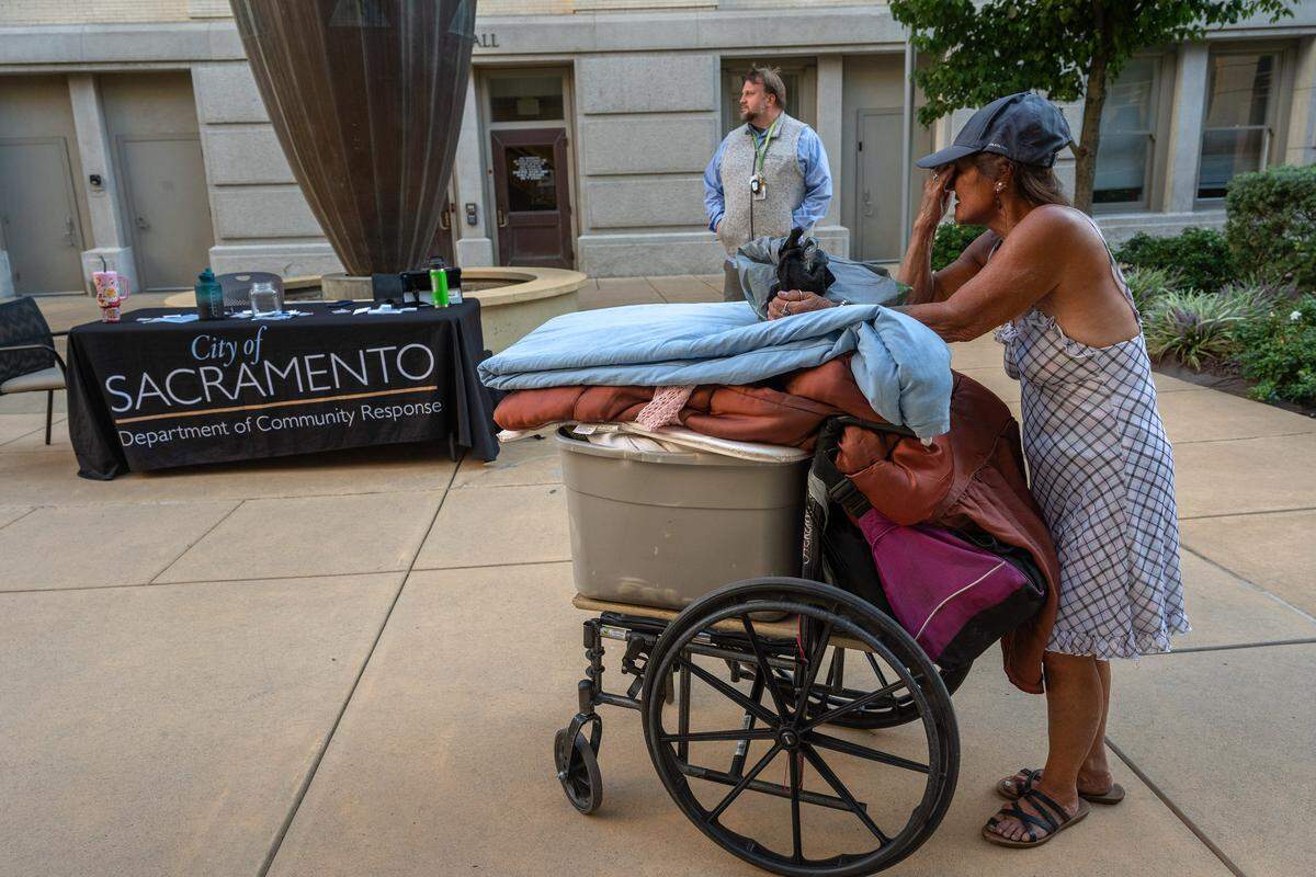 Robin Elizabeth Williams shows signs of stress as she waits to meet with a Sacramento Department of Community Response staffer on Wednesday, the night before the ordinance banning camping at City Hall took effect. DCR programs manager Hezekiah Allen, in the background, said the city had beds at its Outreach and Engagement Center for people who sleep at City Hall. Many declined the offer, citing the center's distance, curfews and restrictions on pets and storage.