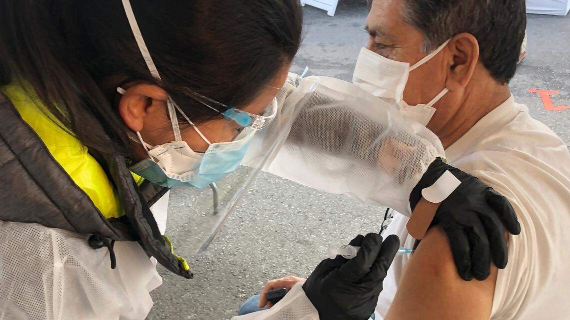 Juan Delgado, 73, right, receives a COVID-19 vaccine shot from a health care worker at a vaccination site in the Mission district of San Francisco, Monday, Feb. 8, 2021. Counties in California and other places in the U.S. are trying to ensure they vaccinate people in largely Black, Latino and working-class communities that have borne the brunt of the coronavirus pandemic. (AP Photo/Haven Daley)