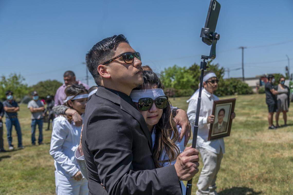 Trang Nguyen is comforted by her brother Jason Le after handing over the live stream camera to him during her father-in-law Dung Tan Nguyen’s funeral in Sacramento on Wednesday, May 6, 2020, during the coronavirus outbreak.”I was crying for three days. It was a lot of stress. I would have hired a photographer and videographer,” said Nguyen. At right her husband Bao Nguyen holds a picture of his father.