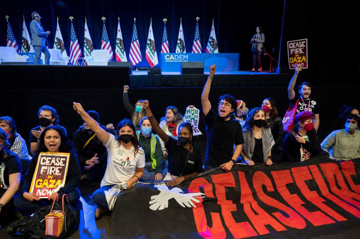 Demonstrators calling for a cease-fire in the Israel-Hamas war sit in front of the stage, disrupting the afternoon session at the Democratic nominating convention Saturday at SAFE Credit Union Convention Center.