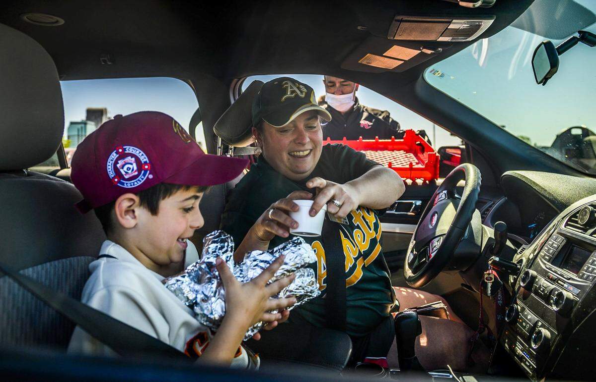 Ryan Stockbridge, left, excitedly holds a pile of hotdogs as his mother Melissa Stockbridge hands him ice cream as the Sacramento River Cats sell $1 hot dogs, ice cream, and soda and $4 cans of beer to fans in celebration of what would have been their season home opener, Tuesday, April 14, 2020, in a drive thru at Sutter Health Park in West Sacramento.