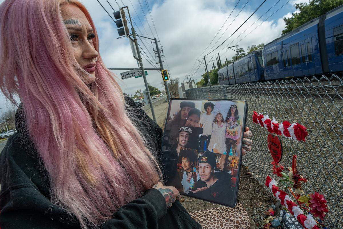 Erika Pringle, 37, holds photos of her brother, Andrew Pringle, as she looks in March toward the light rail he had hoped to catch in 2023 when he was struck by a motorist who ran a red light at the intersection of Folsom Blvd. and Manlove Road in Rosemont. Andrew died later that night in the hospital.