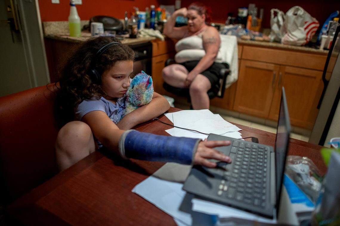 Aryanna Slain, 8, holds her stuffed animal as she operates her computer with her broken arm on Friday May 28, 2021 in Sacramento. Her mother Kristi Philips takes a break while making mashed potatoes and pork chops for dinner in the Residence Inn by Marriott hotel they are now staying. Her hope is to someday live in a house but for the past year they have been living in hotel rooms and a camper they own when they are unable to pay for hotels.