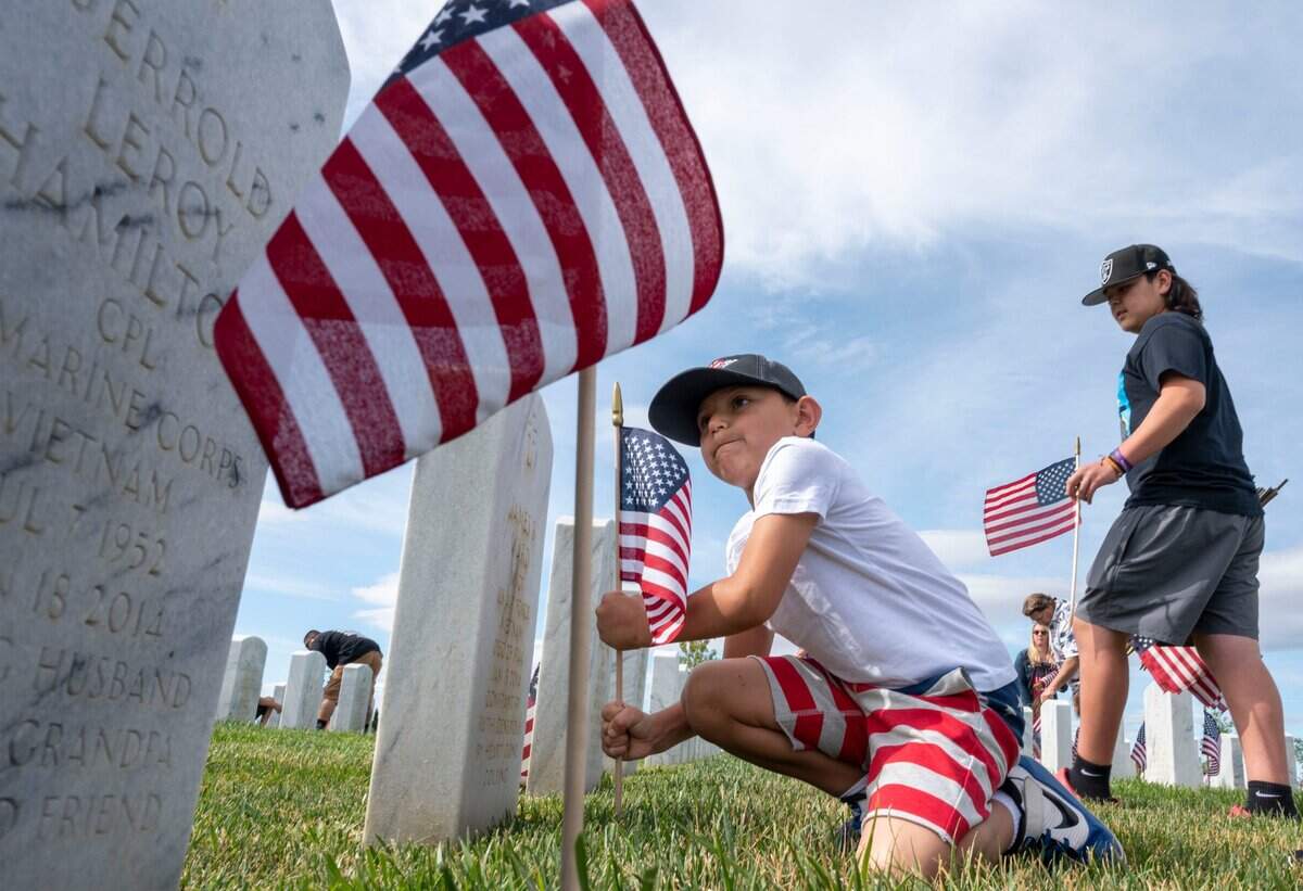 Derrick Garcia, 6, of Winters, uses his might to place a lawn flag as his family, including brother Anthony, 12, right, put flags in front of headstones at the Sacramento Valley National Cemetery in Dixon as part of the Memorial Day ceremony Saturday. The ceremony returned to in-person after a two-year COVID-19 hiatus.