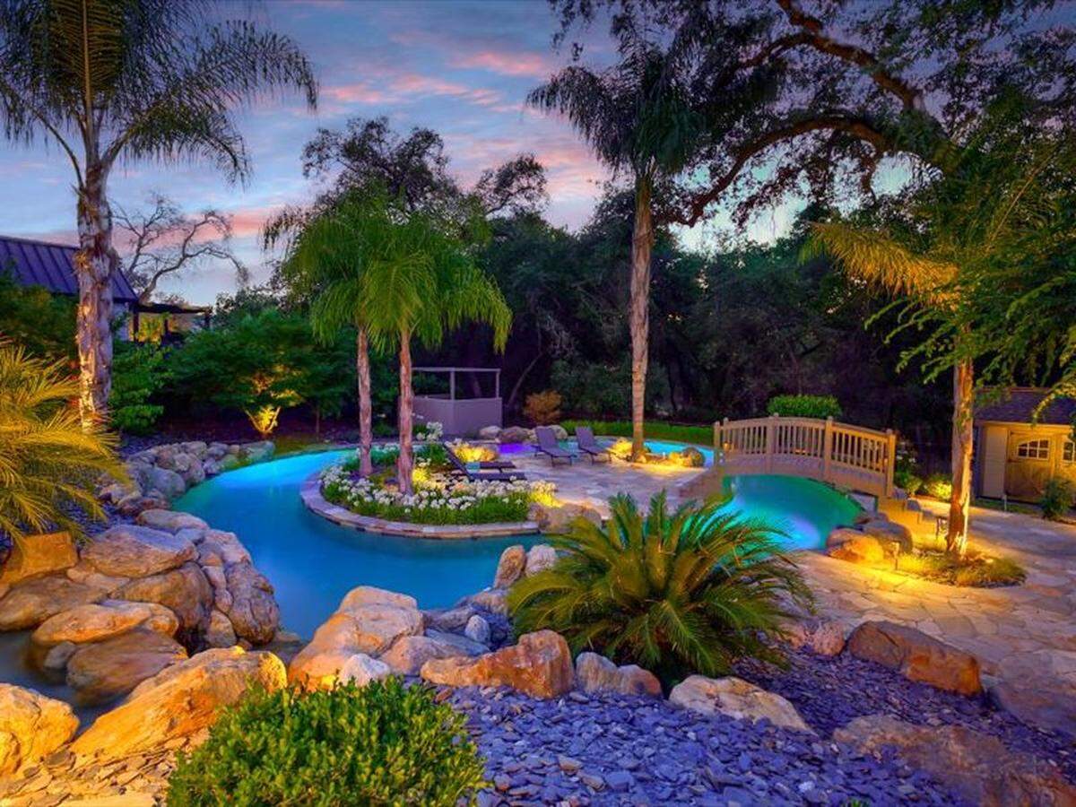 A bridge takes you to a sitting area surrounded by the lazy river. The backyard also offers a hot tub, fire pit lounge and covered pavilion.