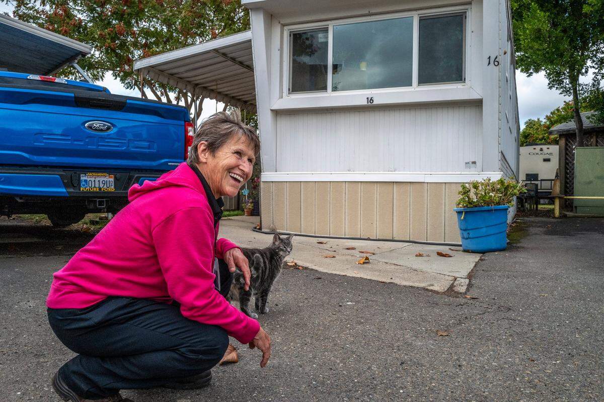 Tracey Knickerbocker pets Demos, the neighbor’s cat, who she says greets her every afternoon when she returns to the home she purchased for $2,000 in a mobile home park for seniors over age 55. She credits her faith in God and the kindness of others for helping her get off the streets.