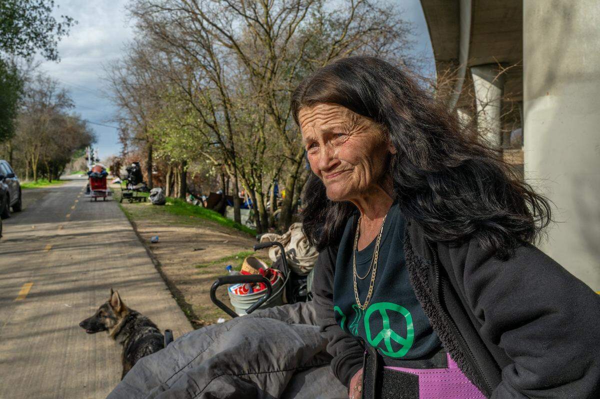 Renée VanVliet, 59, recovering from pneumonia, sits Wednesday on the Sacramento Northern Bike Trail in North Sacramento, alongside her belongings and one of her four dogs during a homeless sweep of an encampment she had been living in for the past three years.