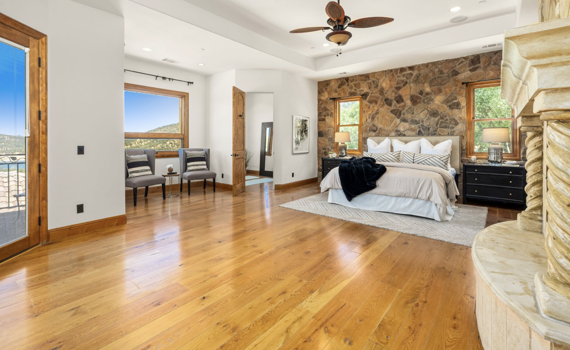 The serene primary suite on the main level offers a rock accent wall, spa-inspired bath, direct terrace access, and inspiring lake views.