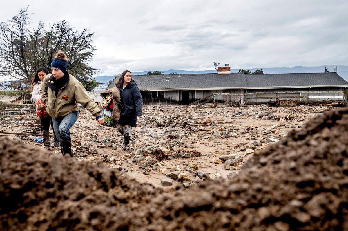 Hana Mohsin, right, carries belongings from a neighbor’s home which was damaged in a mudslide on Wednesday, Jan. 27, 2021, in Salinas, Calif. The area, located beneath the River Fire burn scar, is susceptible to landslides as heavy rains hit hillsides scorched during last year’s wildfires.