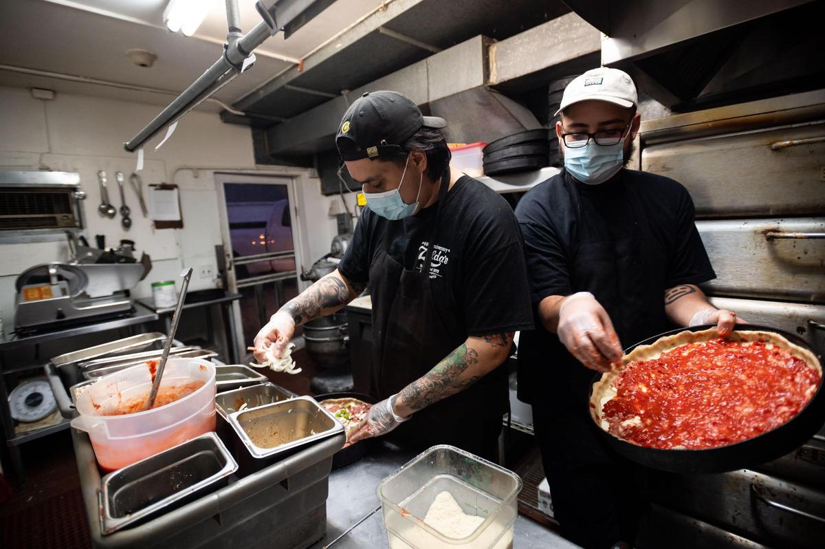 Pizza cook Christian Moreno, right, walks around another cook to add toppings to a Chicago-style deep dish pie in the small kitchen at Zelda’s Original Gourmet Pizza on Dec. 22, 2020, in midtown Sacramento. The restaurant has since closed.