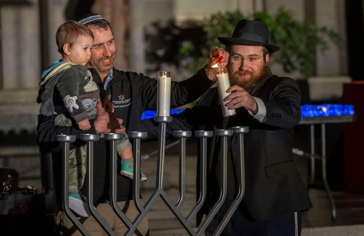 Rabbi Matt Rosenberg, center, holds his son Solomon Rosenberg, 1, while lighting a menorah with Rabbi Moshe Cohen during a Hanukkah celebration by Chabad Greater Sacramento on Thursday at the Capitol.