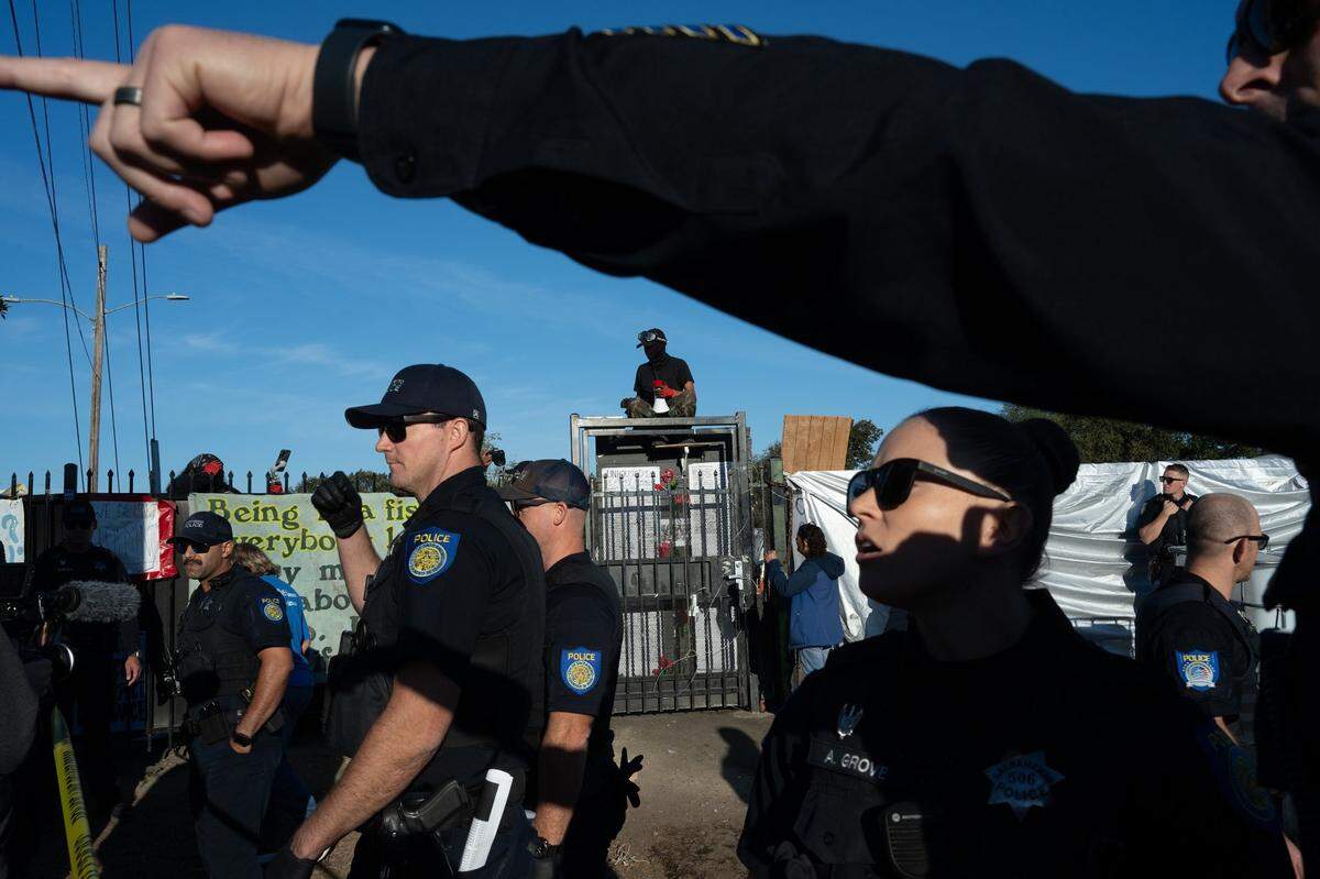 A resident who said he had been living at Camp Resolution the past two years shouts from the top of its gate in protest as Sacramento Police arrive to remove the encampment on Monday, Aug. 26, 2024. The photograph received the fifth-place award in news photography.