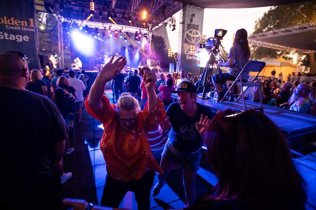 Cynthia Lynch, left, of Sacramento, raises her arms and dances along with a group of fellow fans as Queen Nation, a Queen tribute band, performs Crazy Little Thing Called Love on the Golden 1 Stage during the California State Fair at Cal Expo on Tuesday, July 26, 2022, in Sacramento. Ive seen them in concert, Lynch said of the original band fronted by Freddie Mercury, adding she does not like them, but loves them.