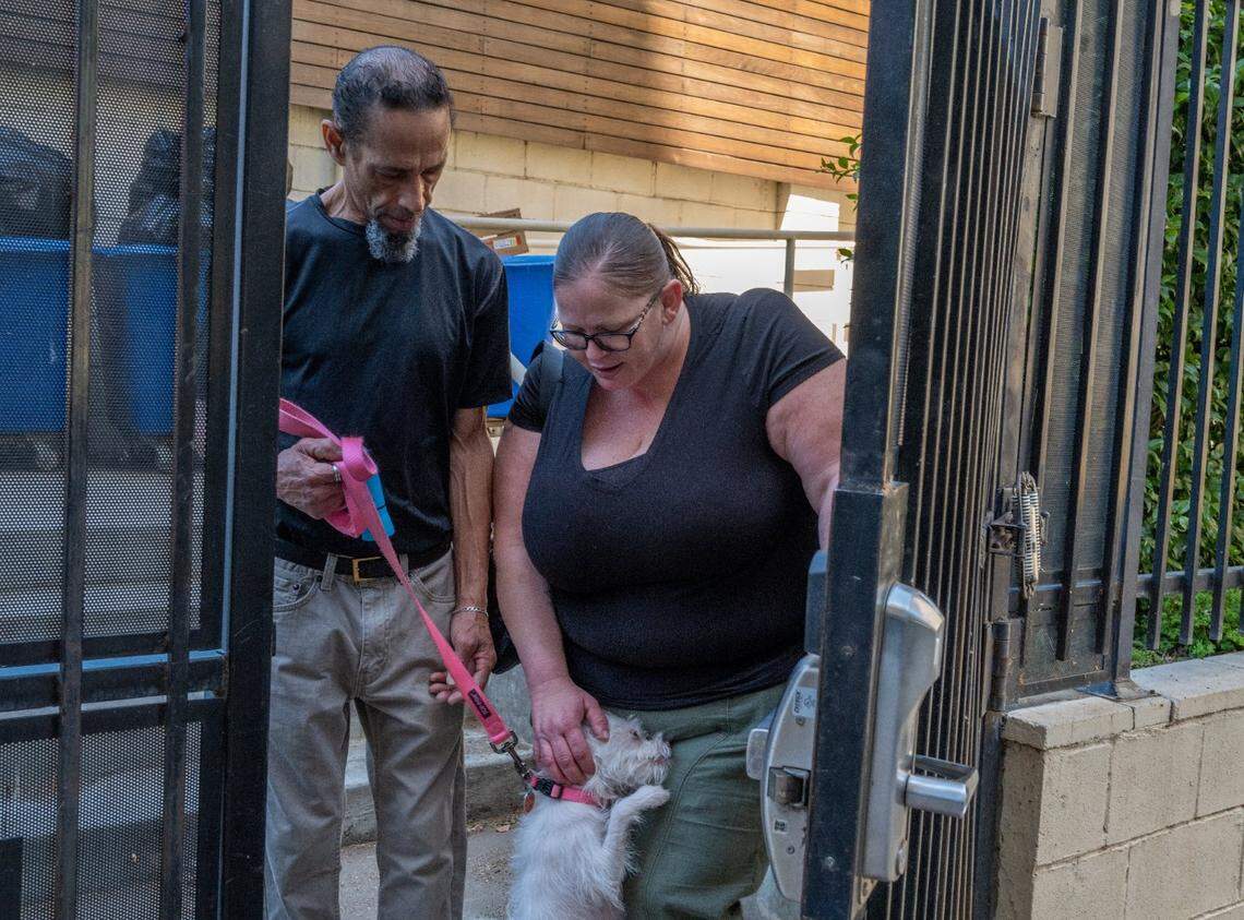 Project Roomkey participants Amber Box-Matson, 37, pets her dog Aphrodite as her boyfriend Edward Aubry, 56, holds her leash at the Vagabond Inn motel in Sacramento on May 17, 2023. Box-Matson works as a waitress at Denny’s, and Aubry as a chef at Pete’s Restaurant and Brewhouse, but they said they can’t afford to live anywhere else on their wages.