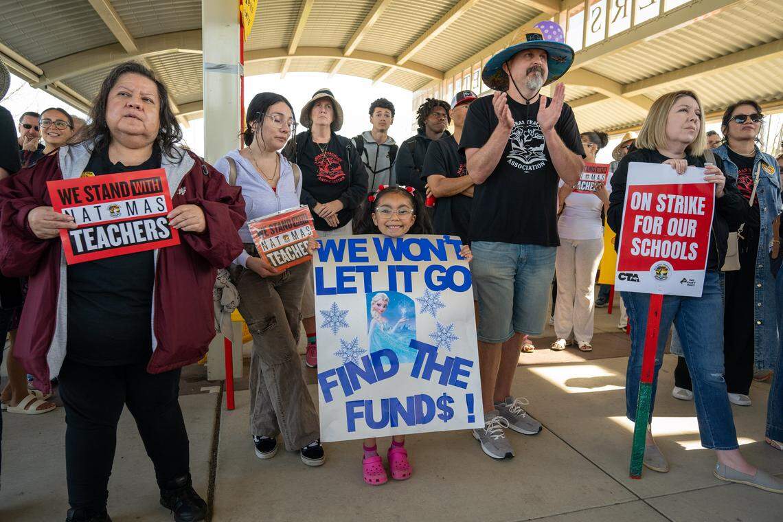 First grade student Catalina Mendoza, 6, center, holds a sign alongside her mother Alondra Mendoza, 28, left, who works as an attendance technician at Natomas High School, during a rally in support of striking Natomas school district teachers in North Natomas Regional Park in Sacramento on Tuesday, March 10, 2026.