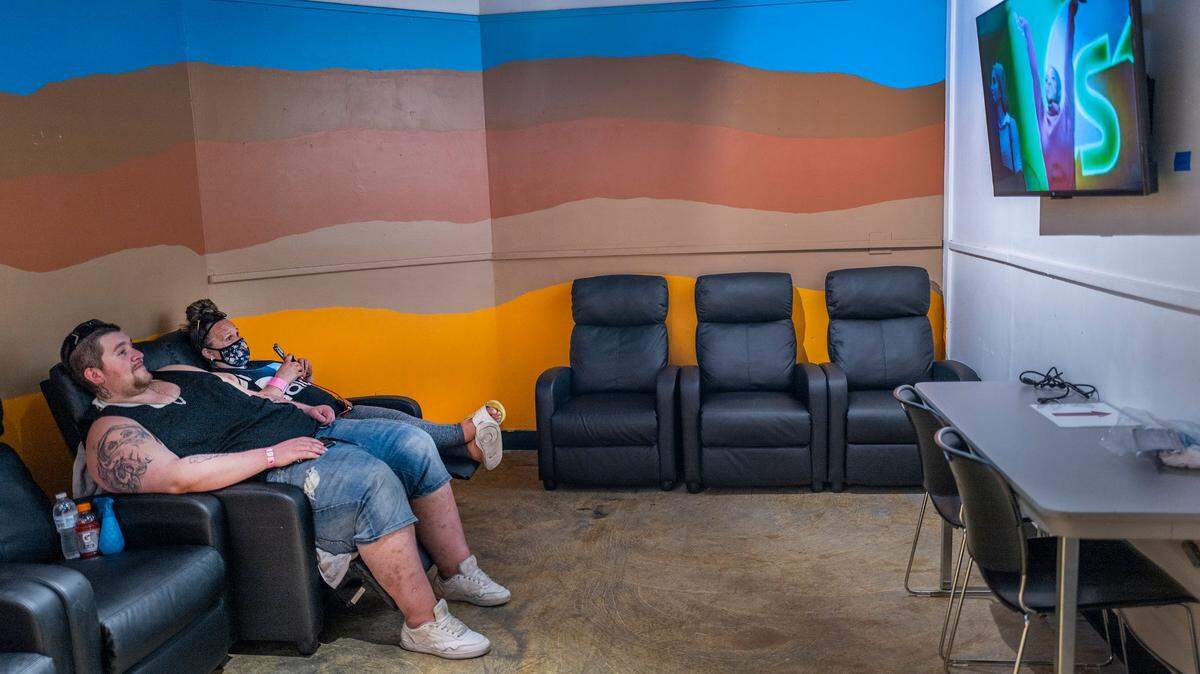 Victor Koutsis, left, and Kristin Goree watch TV as they cool off in the city of Sacramento’s Outreach and Engagement Center at 3515 Auburn Blvd. on July 11, 2022. The city council voted Tuesday to expand the use of warming and cooling centers based on wider extreme weather criteria.