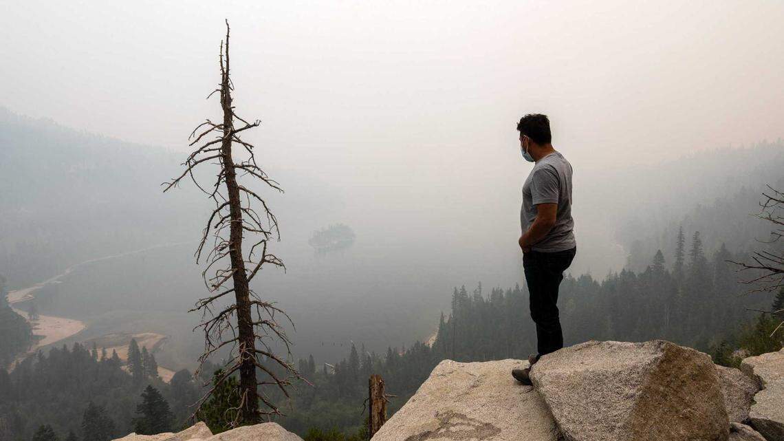 A man vacationing in the Lake Tahoe area stands above Emerald Bay as wildfire smoke from the Caldor Fire obscures Fannette Island in 2021. Researchers at UC Davis say as wildfire activity has grown, the state’s pristine bodies of water have been affected by smoke.