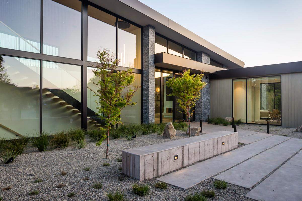 Zen-inspired landscaping creates a tranquil entry, where gravel, mature trees, and artistic lighting welcome residents home.