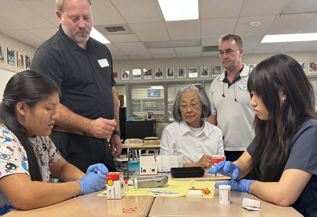 Health Tech students Stephanie Castro, left, and Angelina Tran check to see whether their diagnostic analyzer is working properly. Helping them are Tyler Cheek, the Arizona and California territory manager for PTS Diagnostics, left; volunteer Peggy Kow; and Health Tech coordinator Rodney Black.