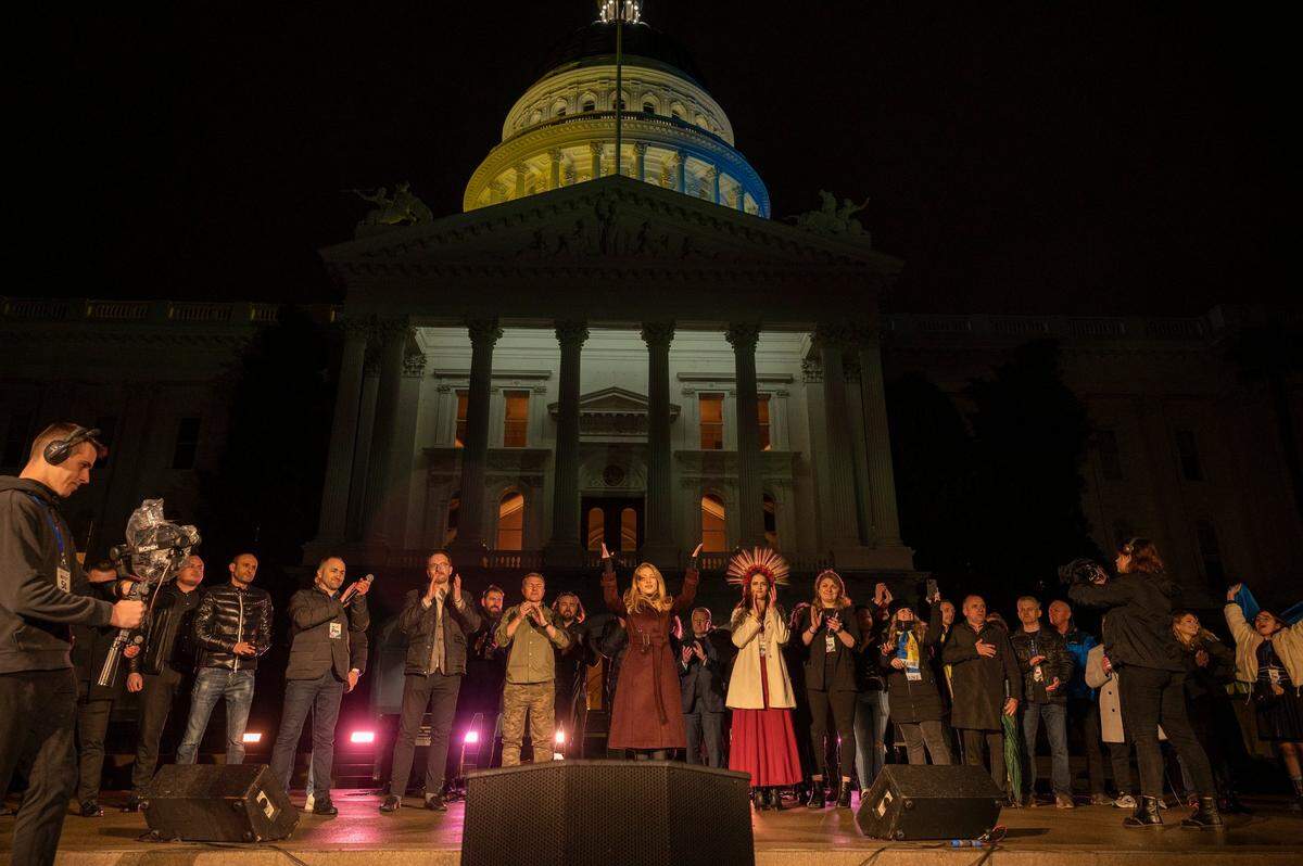 Ukrainian singer Tina Karol, center, is surrounded by speakers and participants at the state Capitol on Friday. The dome was lit with yellow and blue light in solidarity with the Ukraine people.