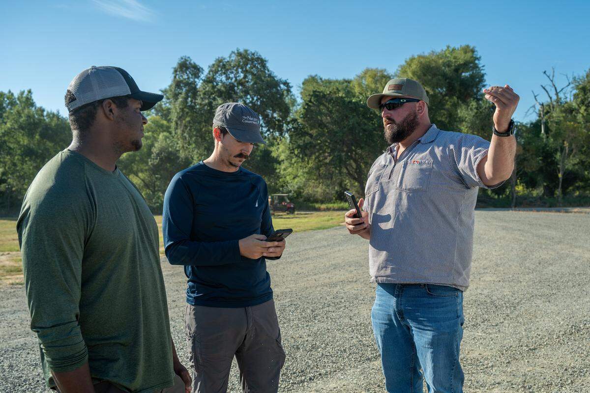 Drake Stallworth, left, and Patrick Carr, center, both with The Nature Conservancy, discuss areas where shorebirds might be migrating with Adam Paul, operations manager at Montna Farms in Sutter County on Aug. 22.