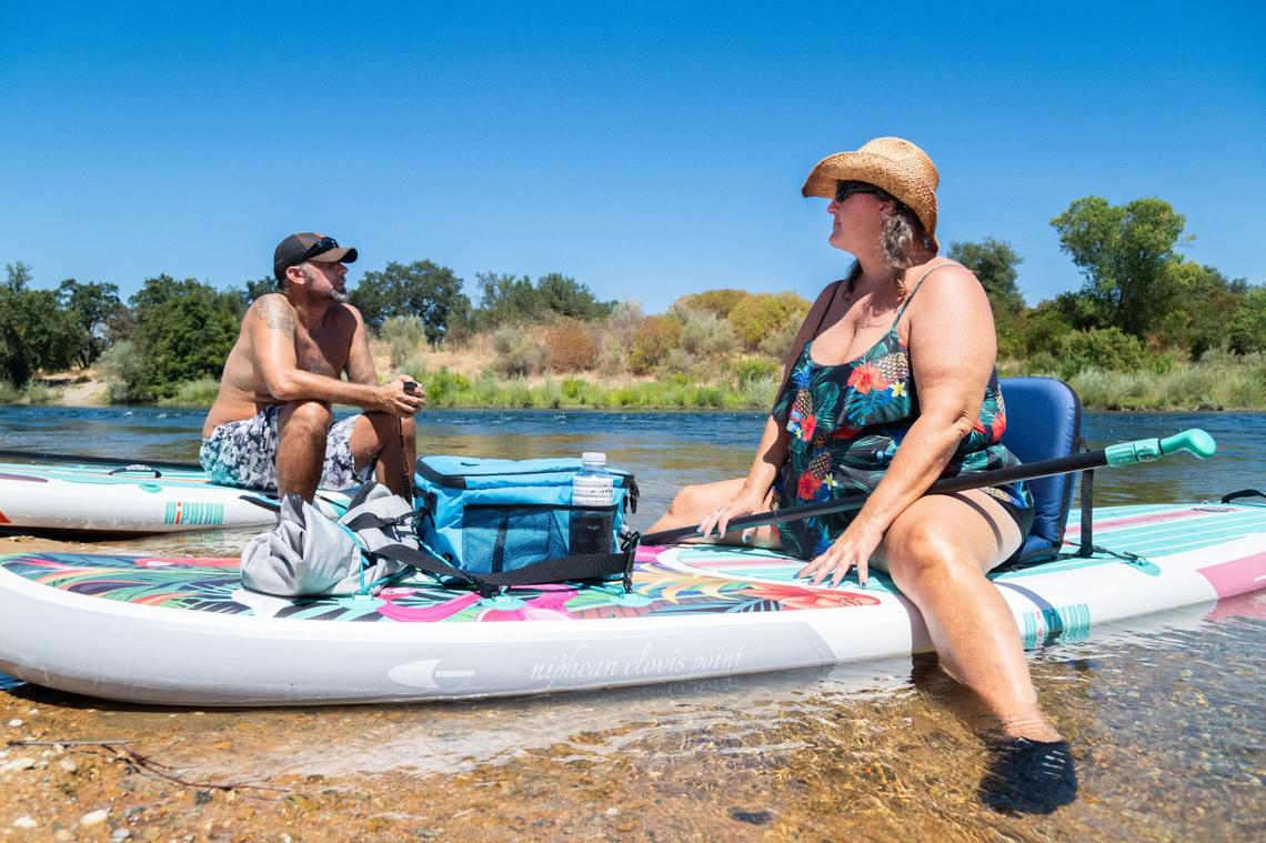 Jeramie Mendoza, left, and Tracy Williams sit on their paddle boards in the water near the clay banks along the American River in Rancho Cordova on Friday, Aug. 9, 2024. “I’m bummed because I love jumping off the clay banks. It’s so much fun. It cools you off,” said Williams about the new signs prohibiting jumping or diving in the area. “This is like the first year there’s been that many deaths, and it’s just, like, I know they have to do something, so it’s a bummer, but I get it.”