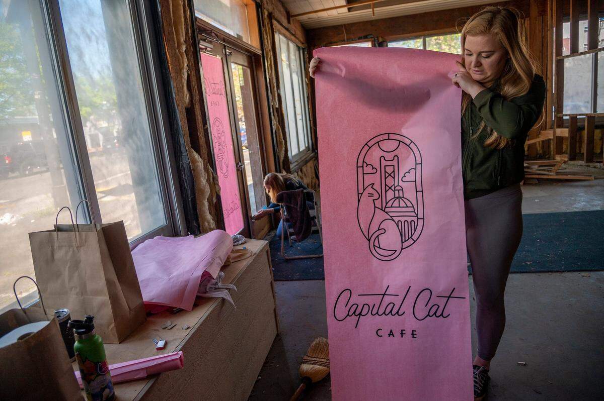 Emalee Ousley, right, who owns Capital Cat Café with her mother Laura Ousley, left, prepares to hang a sign inside the cat cafe on Tuesday, March 22, 2022.