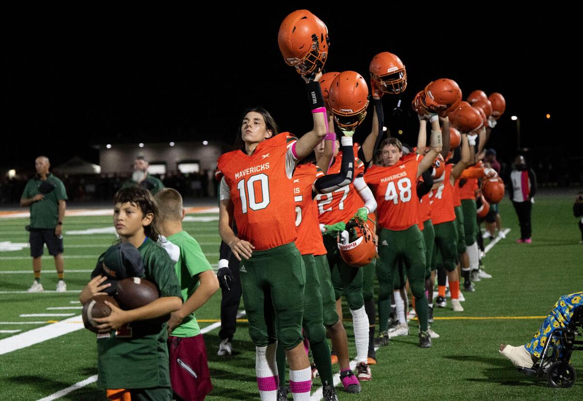 The Mesa Verde High School varsity football team hold up their helmets at the start of their first game at their brand-new football field Friday, a project 40 years in the making.