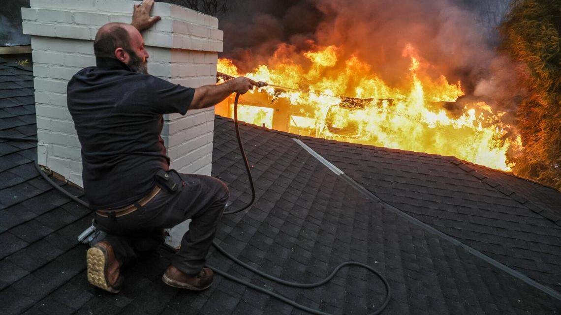 Jimmy Orlandini shields himself from intense heat as he hoses down a neighbors’ rooftop on Sinaloa Avenue in Altadena as the Eaton Fire burns on Wednesday, Jan 8, 2025.