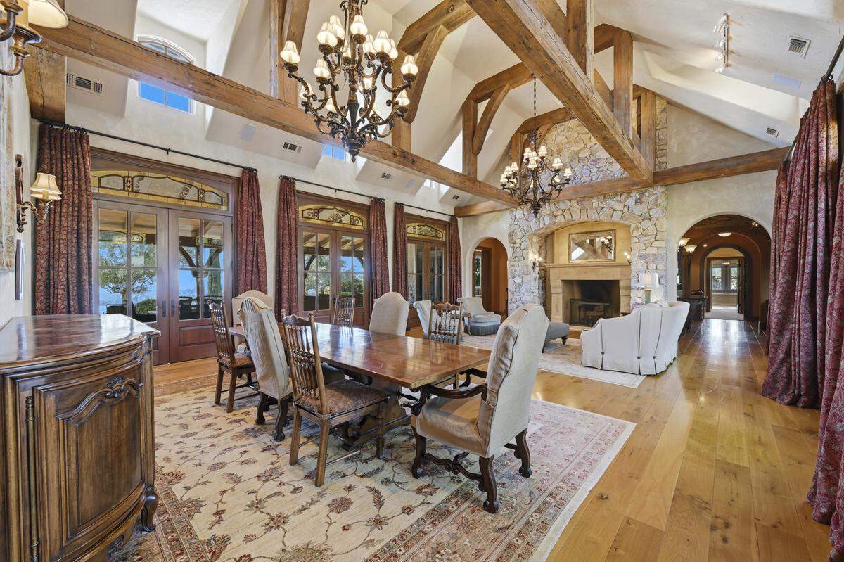 The heart of the house is the soaring great room — the “great hall” — where massive stonework frames a fireplace and salvaged railroad beams span the ceiling.