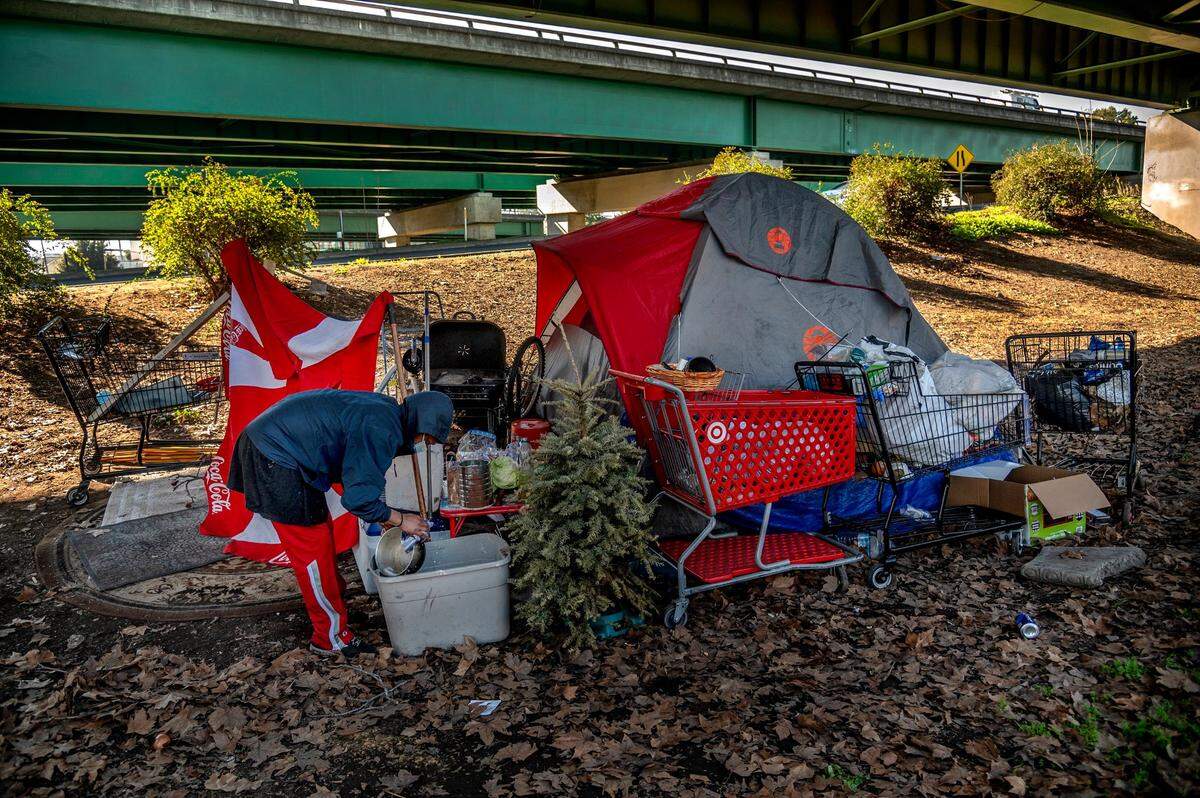 Timell Brown washes dishes next to a dried out Christmas tree outside a tent that she has tried to make home under a freeway interchange near W Street. Brown is one of 1,250 Housing Choice Voucher holders in Sacramento who do not have housing, according to the Sacramento Housing and Redevelopment Agency. The number ticked up from 1,000 two years ago, despite a new state law aimed at making it easier for voucher holders to find housing.