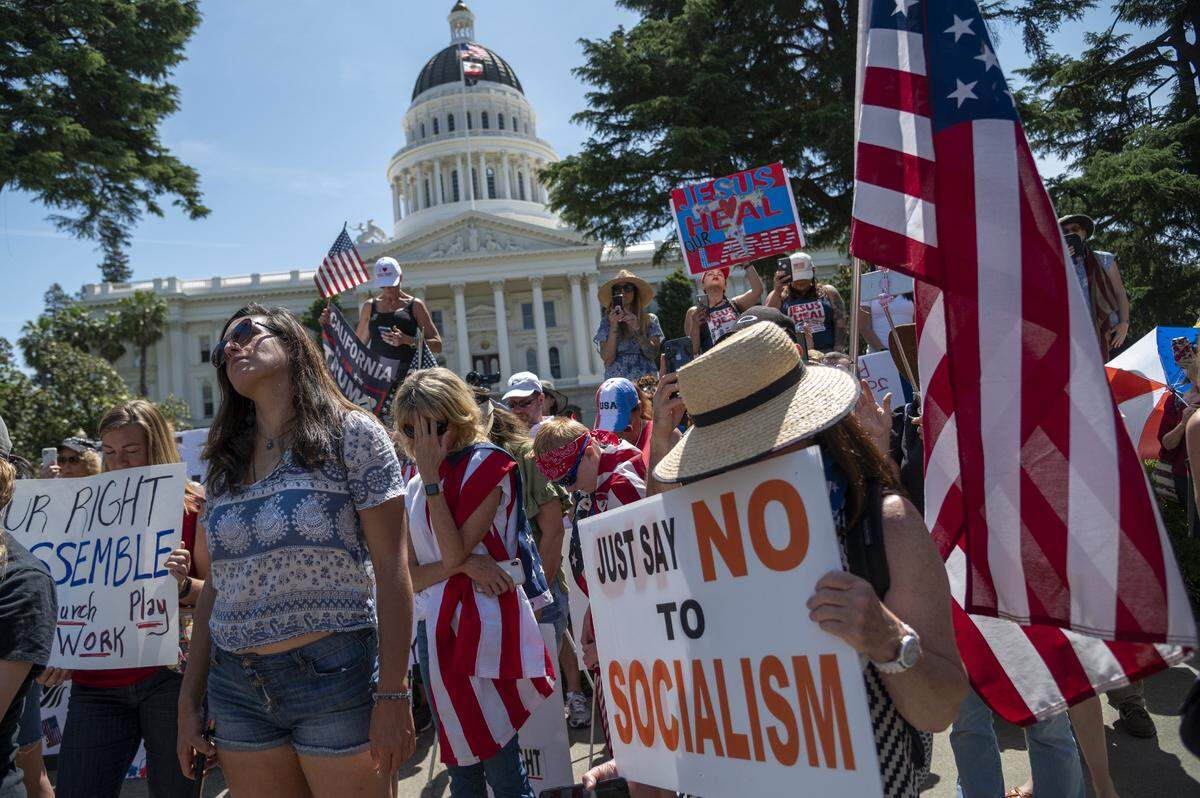 Protesters hold signs on 10th Street in Sacramento as the CHP prevents demonstrators from entering the Capitol grounds on Thursday, May 7, 2020, to rally against Gov. Gavin Newsom’s stay-at-home order during the coronavirus outbreak.