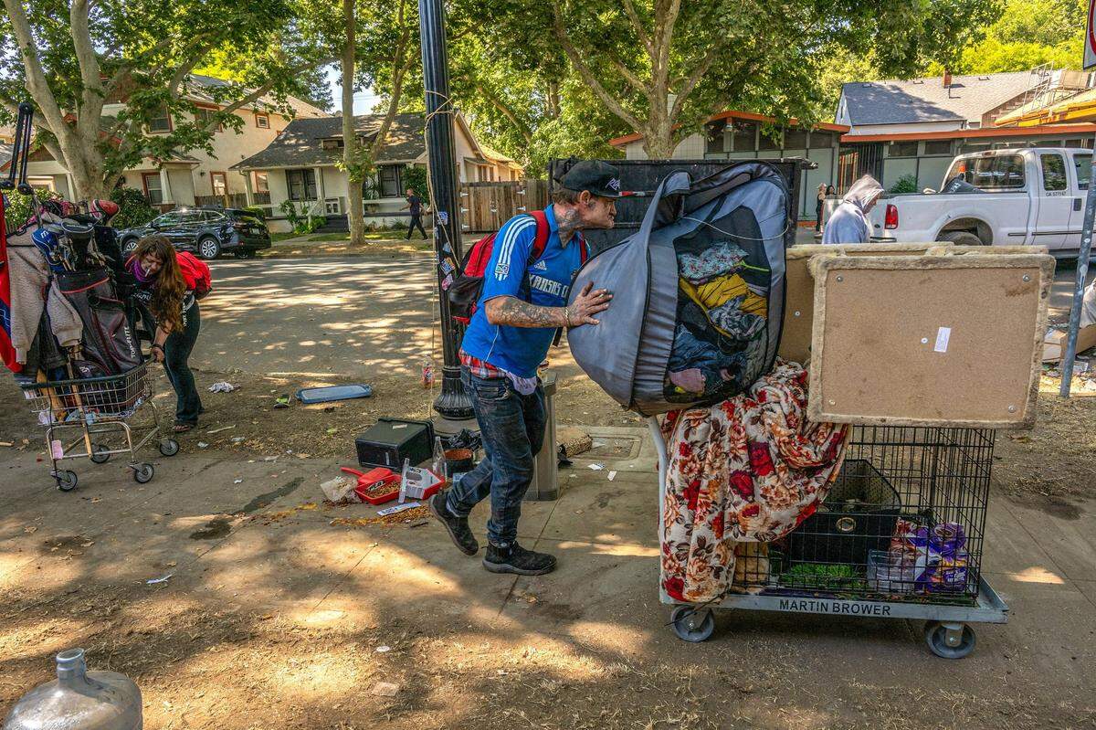 Robert Ash pushes a cart with his belongings, including his cat Meow Meow and dog Sugar, followed by his wife Candice Montoya, left, while city crews sweep a homeless encampment on C street on Wednesday, July 19, 2023. They moved all the belongings they could a few blocks away because they were afraid the workers would discard them.