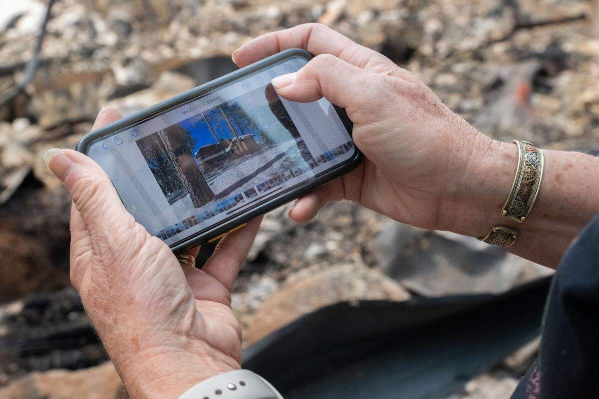 Linda Fischer uses her cellphone to look a photos of her Forest Ranch home, before it was destroyed by the Park Fire, on Wednesday. A photo from March 2023, showing her three-story home blanketed in snow, is displayed.
