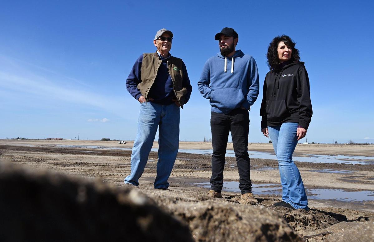 Jennifer Peters of Markarian Family LP, right, with Robert Markarian, left, and Kevin Markarian, center, representing three generations, stand along the edge of a 20-acre basin on their land that the Central Valley family business has dedicated to a National Resources Conservation Service project in hopes of recharging the local aquifer. The recharging basin is adjacent to another 20 acres for a future basin. Photographed Friday, March 3, 2023 near Madera.